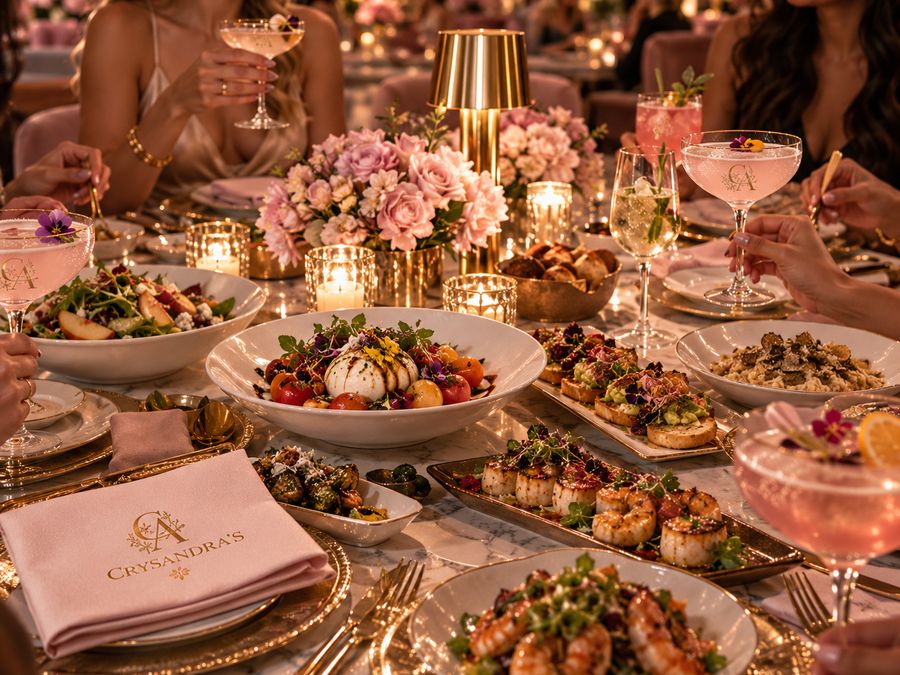 A long table of shareable plates and cocktails with guests gathered around it.